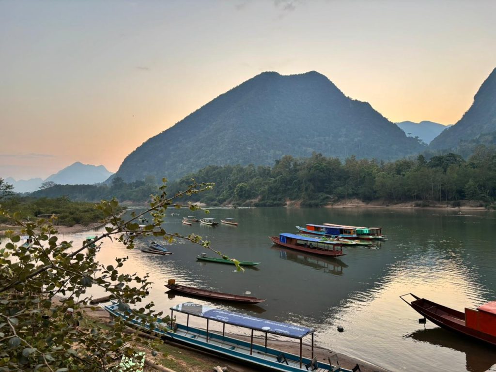 A tranquil village along the Nam Ou River in Laos. With lush mountains, serene waters, and traditional wooden boats, it captures the essence of peaceful rural life.